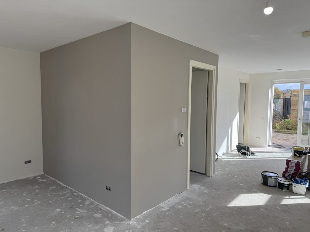 Open nieuwbouwbenedenverdieping met een grijs gesausde wand, witte muren en verfemmers op de dekvloer