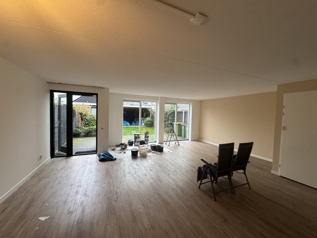 Ruime woonkamer met lichte wanden, een pvc-vloer en schuifpuien naar de tuin tijdens het afwerken